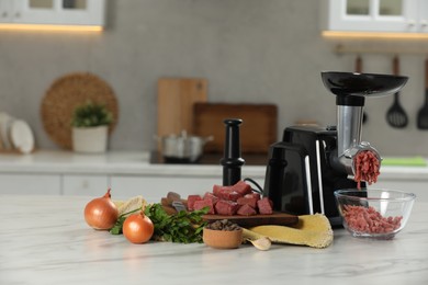 Electric meat grinder with beef mince and products on white table in kitchen