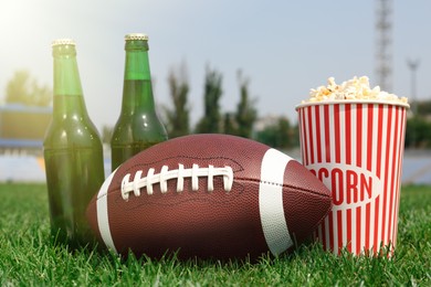 Photo of American football ball with beer and popcorn on green field grass in stadium
