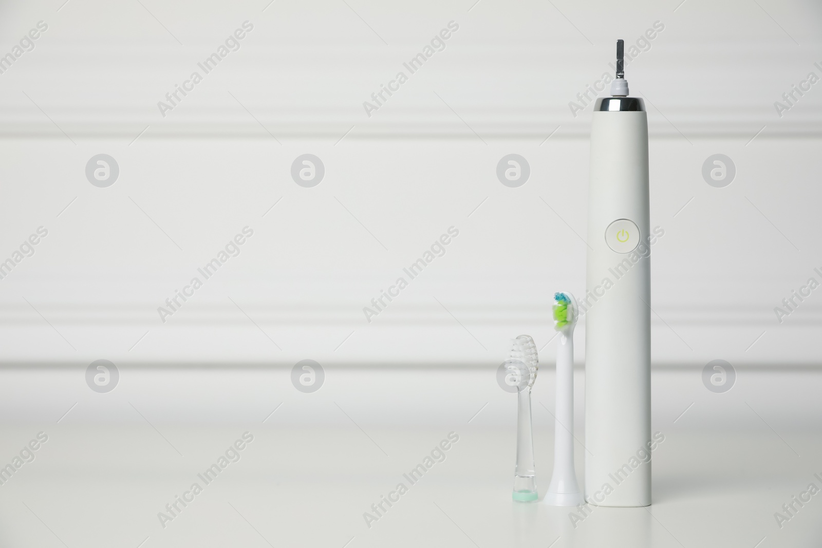 Photo of Electric toothbrush and replacement brush heads on white background, space for text