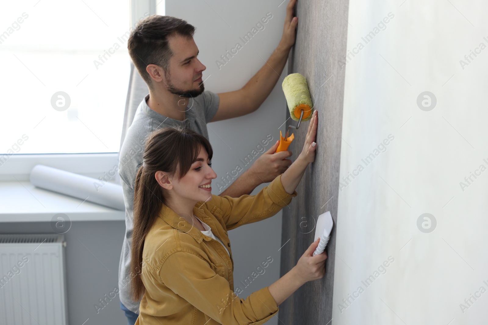 Photo of Couple hanging stylish gray wallpaper in room