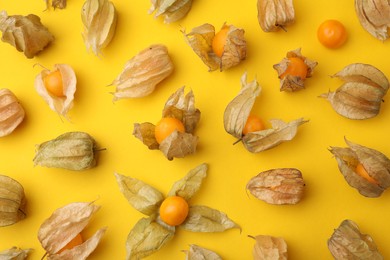 Photo of Ripe physalis fruits with calyxes on yellow background, flat lay