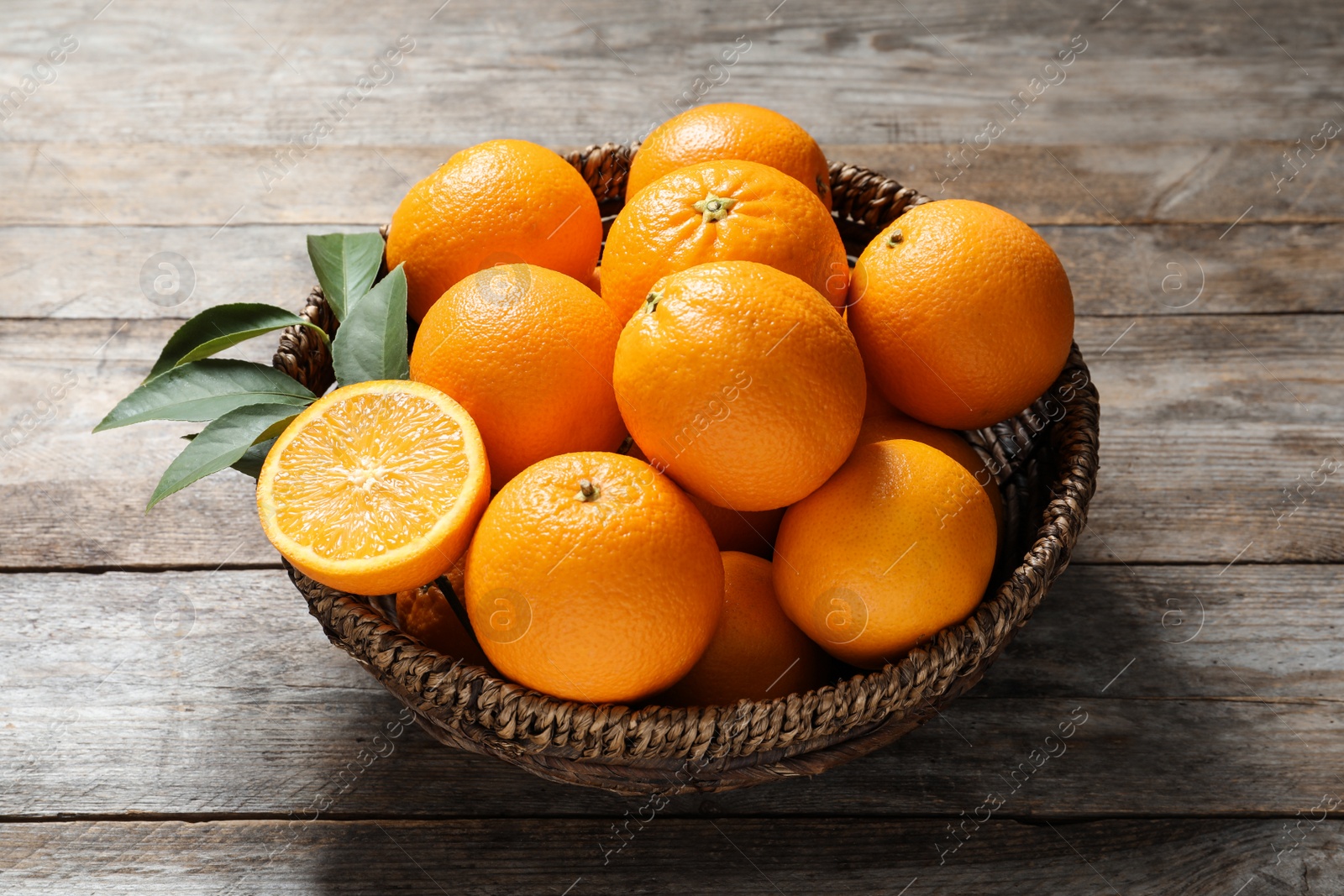 Photo of Wicker bowl with ripe oranges on wooden background