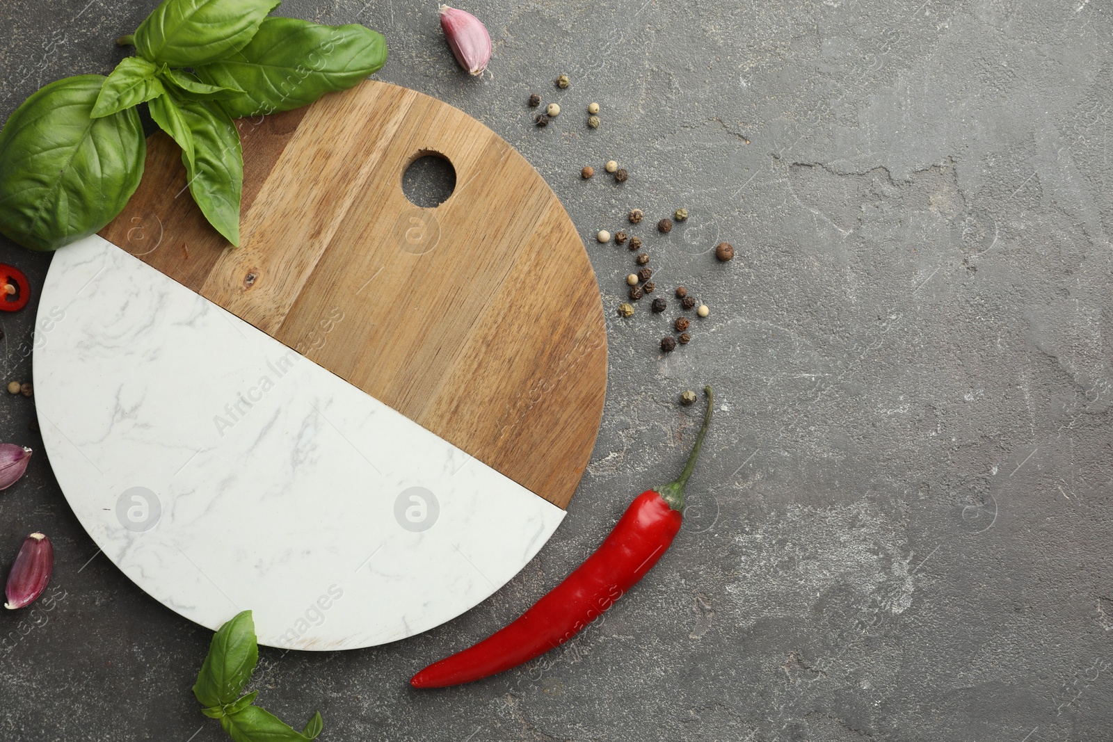 Photo of Cutting board, basil, pepper, chili peppers and garlic on grey table, flat lay. Space for text