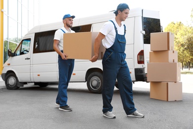 Photo of Male movers unloading boxes from van outdoors