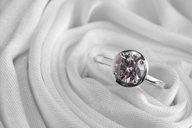 Beautiful engagement ring in white fabric, closeup view. Space for text