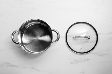 Steel pot and glass lid on white marble table, flat lay