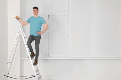 Photo of Young handsome man with roller on stepladder indoors. Room renovation