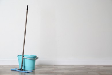 Mop and plastic bucket on floor indoors, space for text. Cleaning service