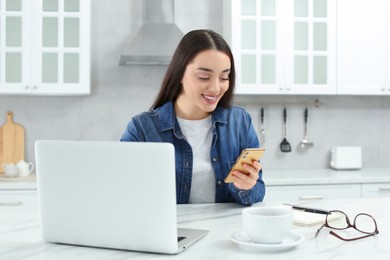 Photo of Home workplace. Woman with smartphone at marble desk in kitchen