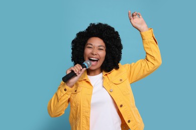 Beautiful woman with microphone singing on light blue background