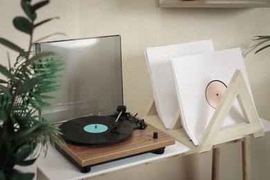 Stylish turntable with vinyl record on wooden table in room