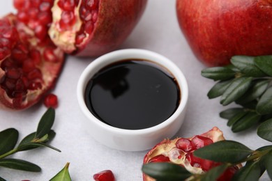 Tasty pomegranate sauce in bowl, branches and fruits on light table, closeup