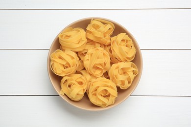 Photo of Raw tagliatelle pasta in bowl on white wooden table, top view