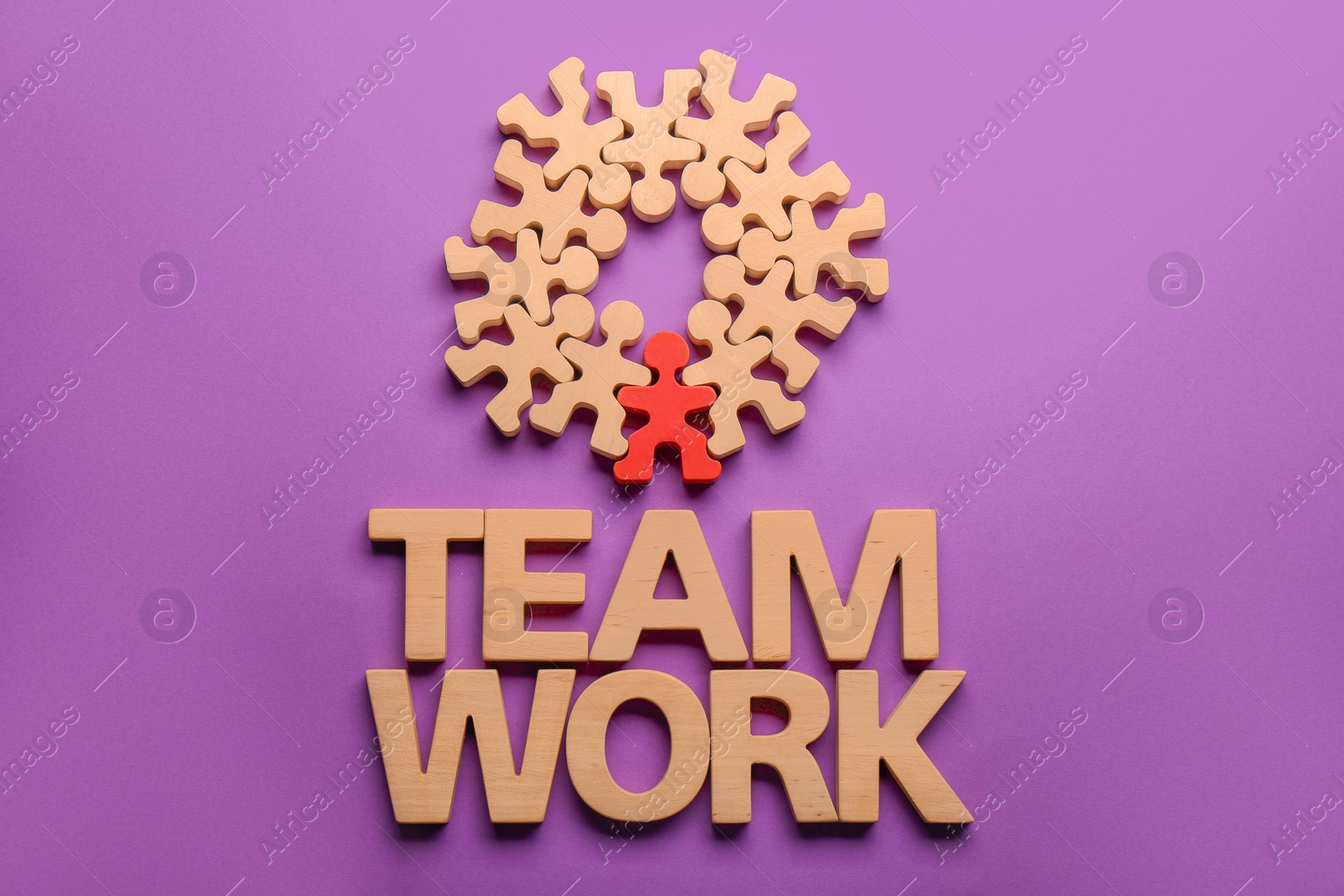 Photo of Words Team Work made of wooden letters, red human figure among others on purple background, flat lay