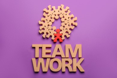 Photo of Words Team Work made of wooden letters, red human figure among others on purple background, flat lay