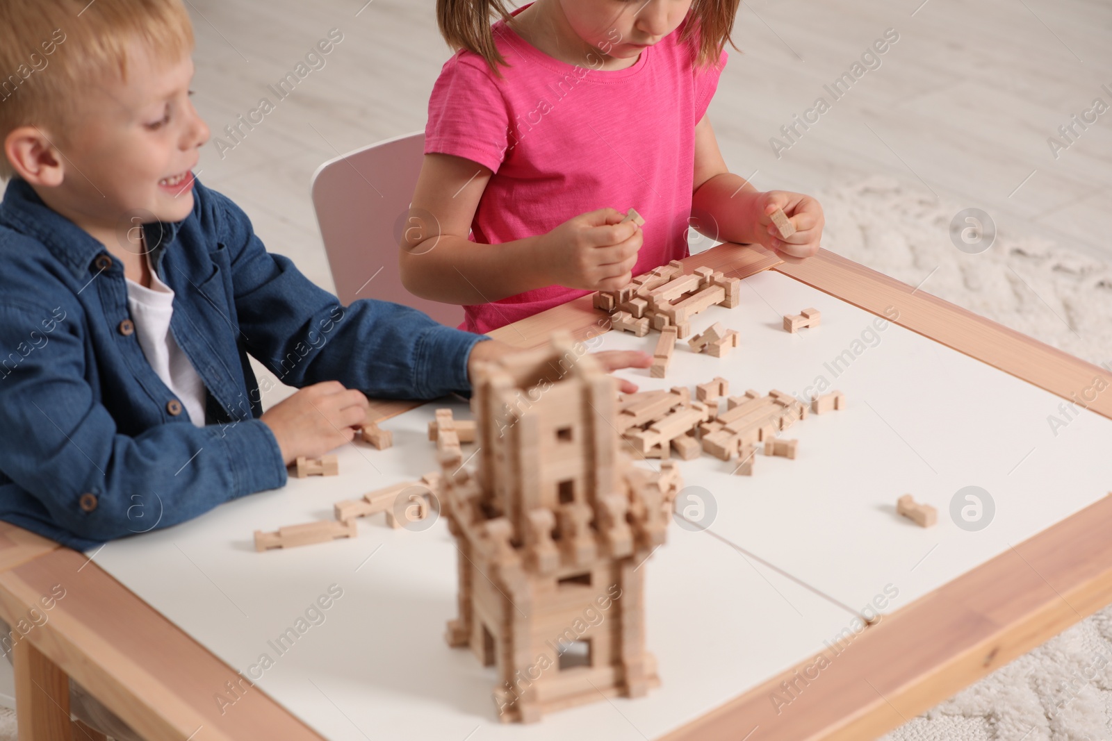 Photo of Little boy and girl playing with wooden tower at table indoors, closeup. Children's toy