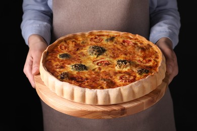 Woman holding delicious homemade vegetable quiche on black background, closeup