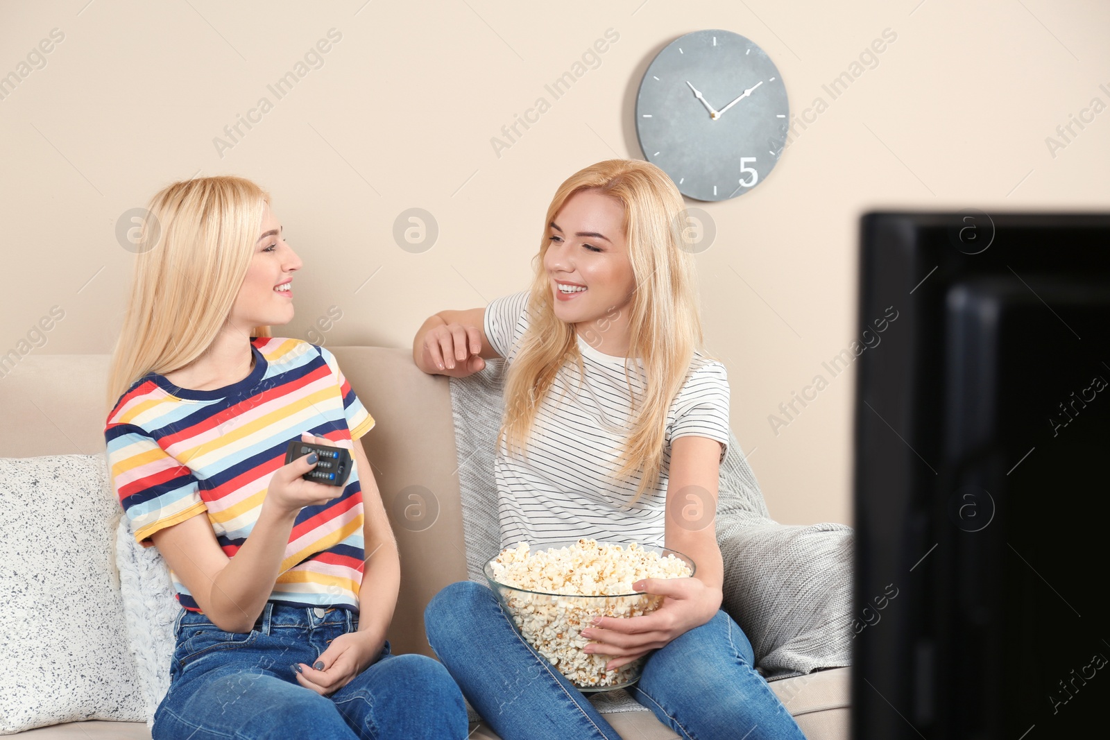 Photo of Young women with bowl of popcorn watching TV on sofa at home