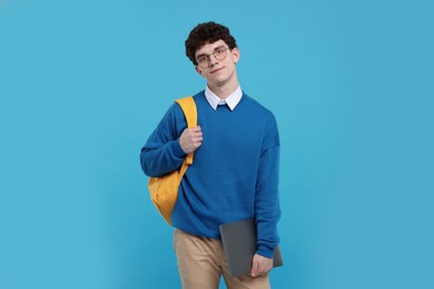 Portrait of student with backpack and laptop on light blue background