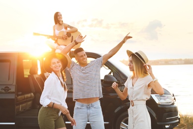 Happy friends having fun near car outdoors at sunset. Summer trip