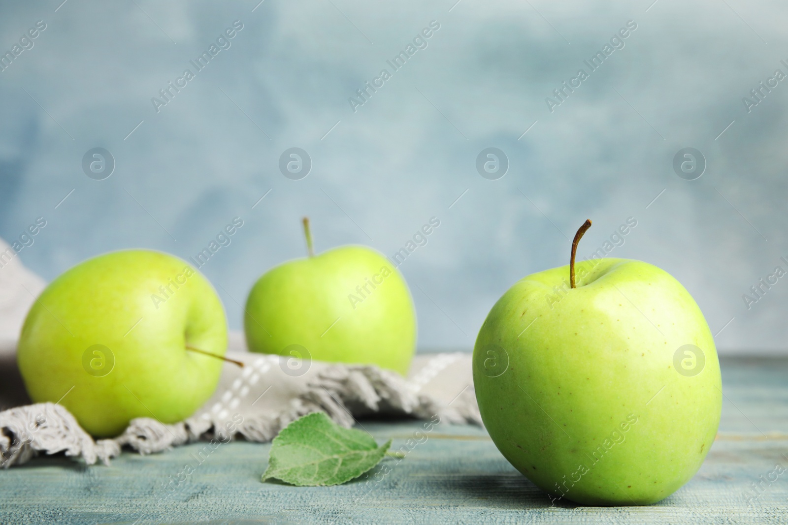 Photo of Fresh ripe green apples on wooden table against blue background, space for text