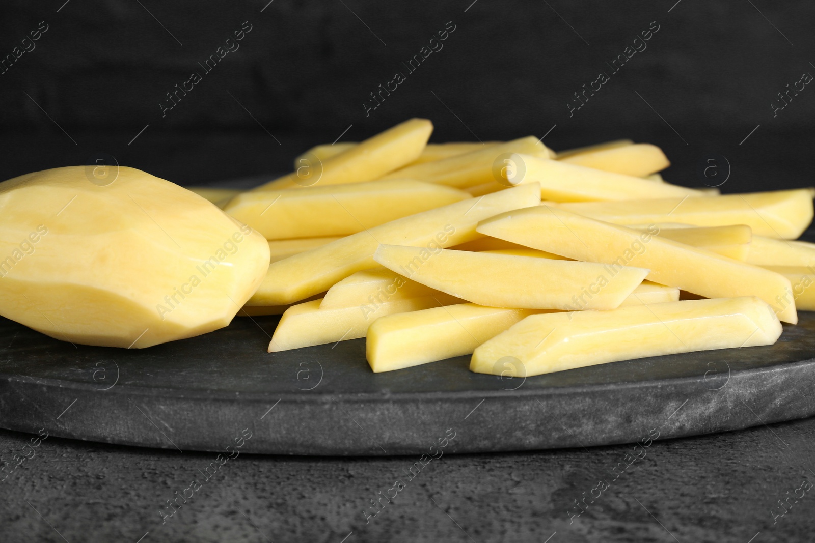 Photo of Whole and cut raw potatoes on grey table, closeup. Cooking delicious French fries