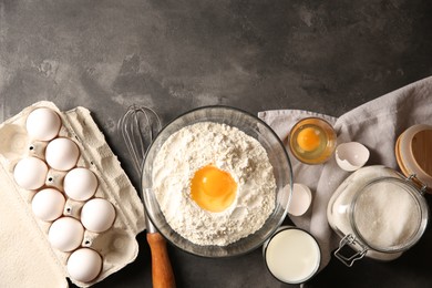 Photo of Making dough. Flour with egg yolk in bowl and other products on grey textured table, flat lay