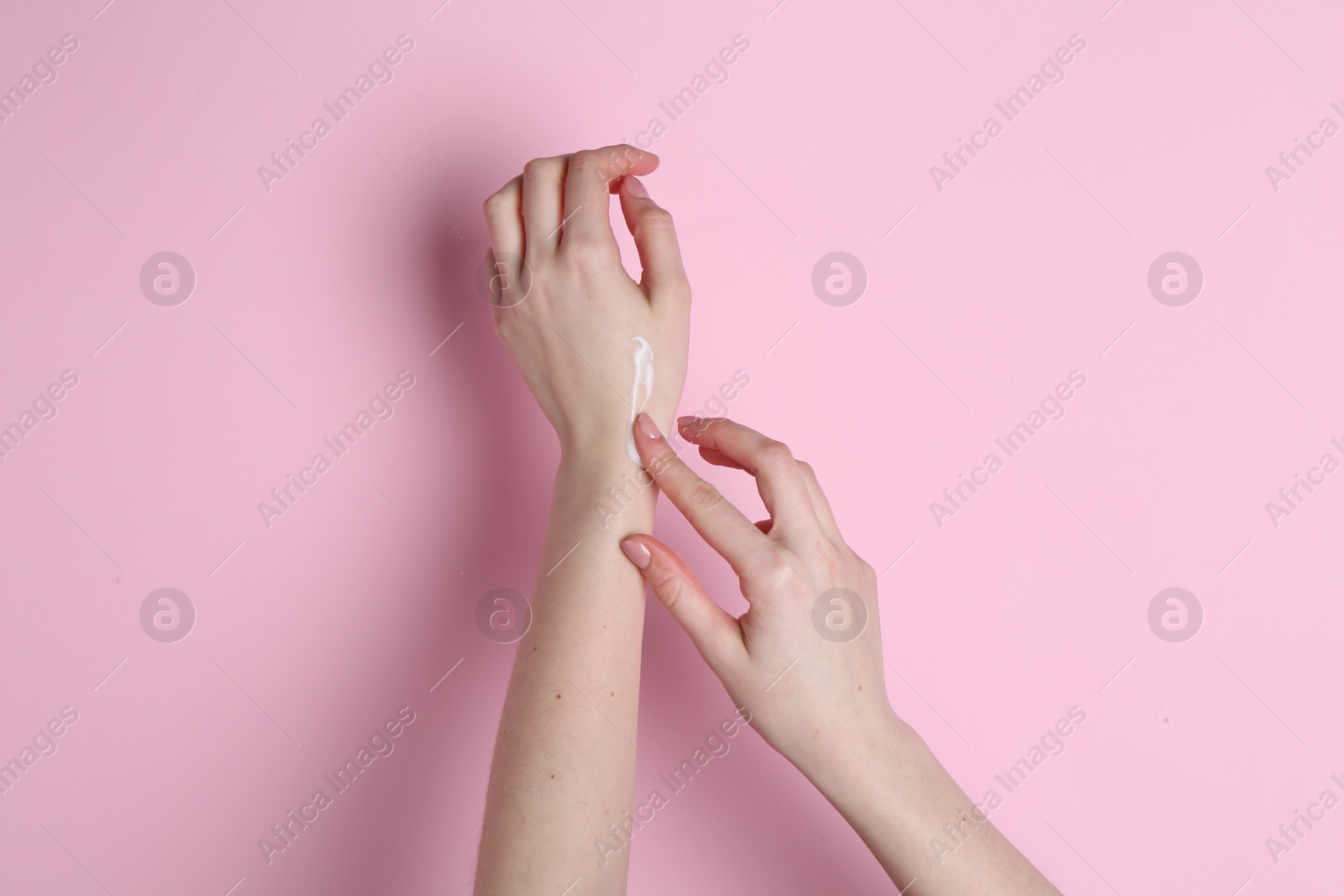 Photo of Woman applying cream on her hand against pink background, closeup