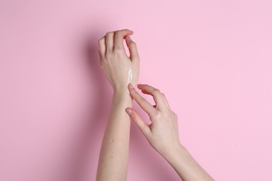 Woman applying cream on her hand against pink background, closeup