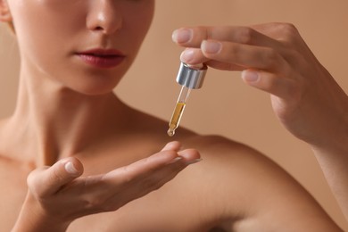 Woman applying cosmetic serum onto her hand on beige background, closeup