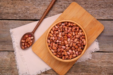 Photo of Bowl and spoon with dry kidney beans on old wooden table, flat lay