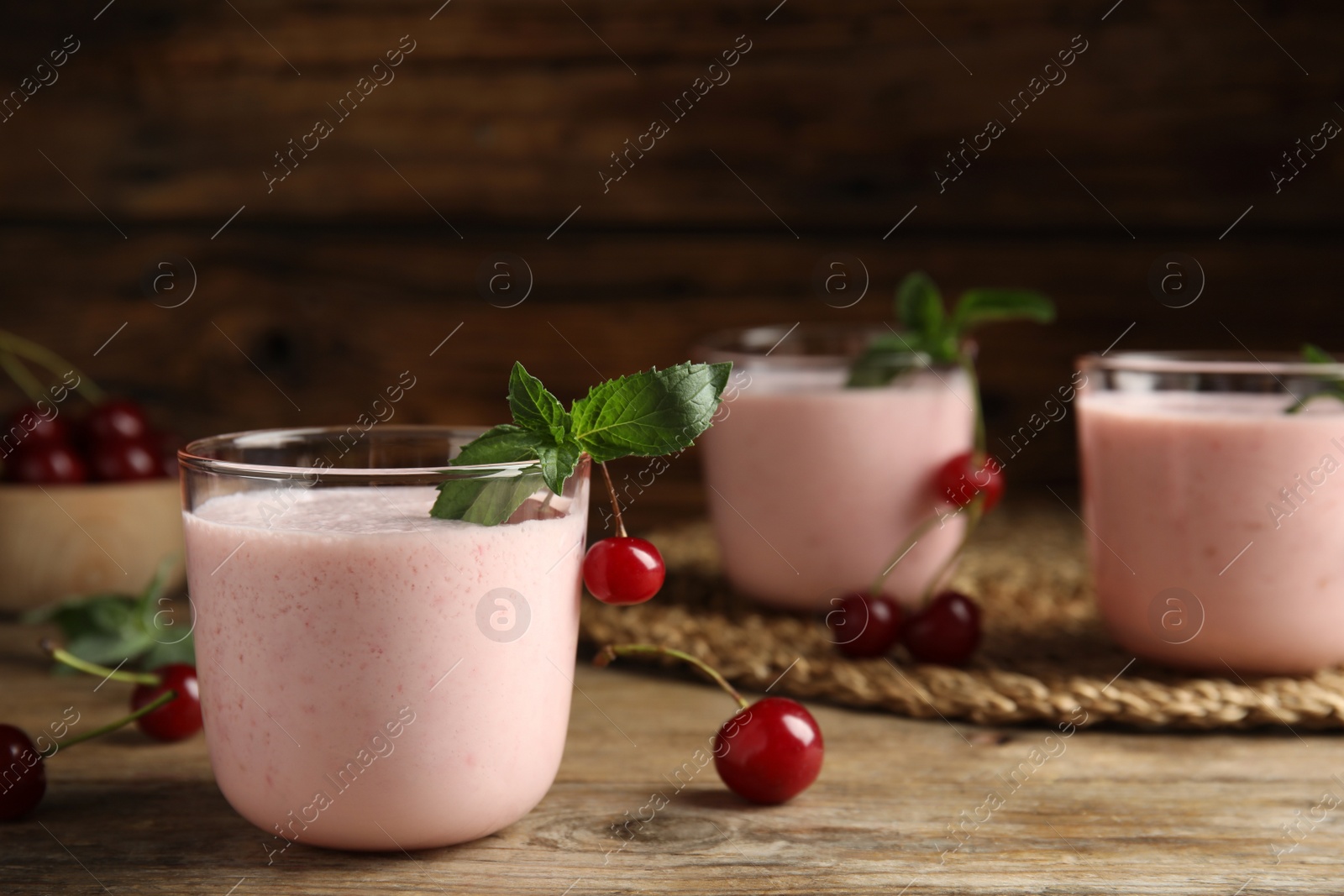 Photo of Tasty fresh milk shake with cherries on wooden table. Space for text