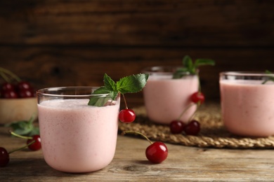 Tasty fresh milk shake with cherries on wooden table. Space for text