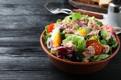 Photo of Bowl of delicious salad with canned tuna and vegetables on black wooden table, space for text