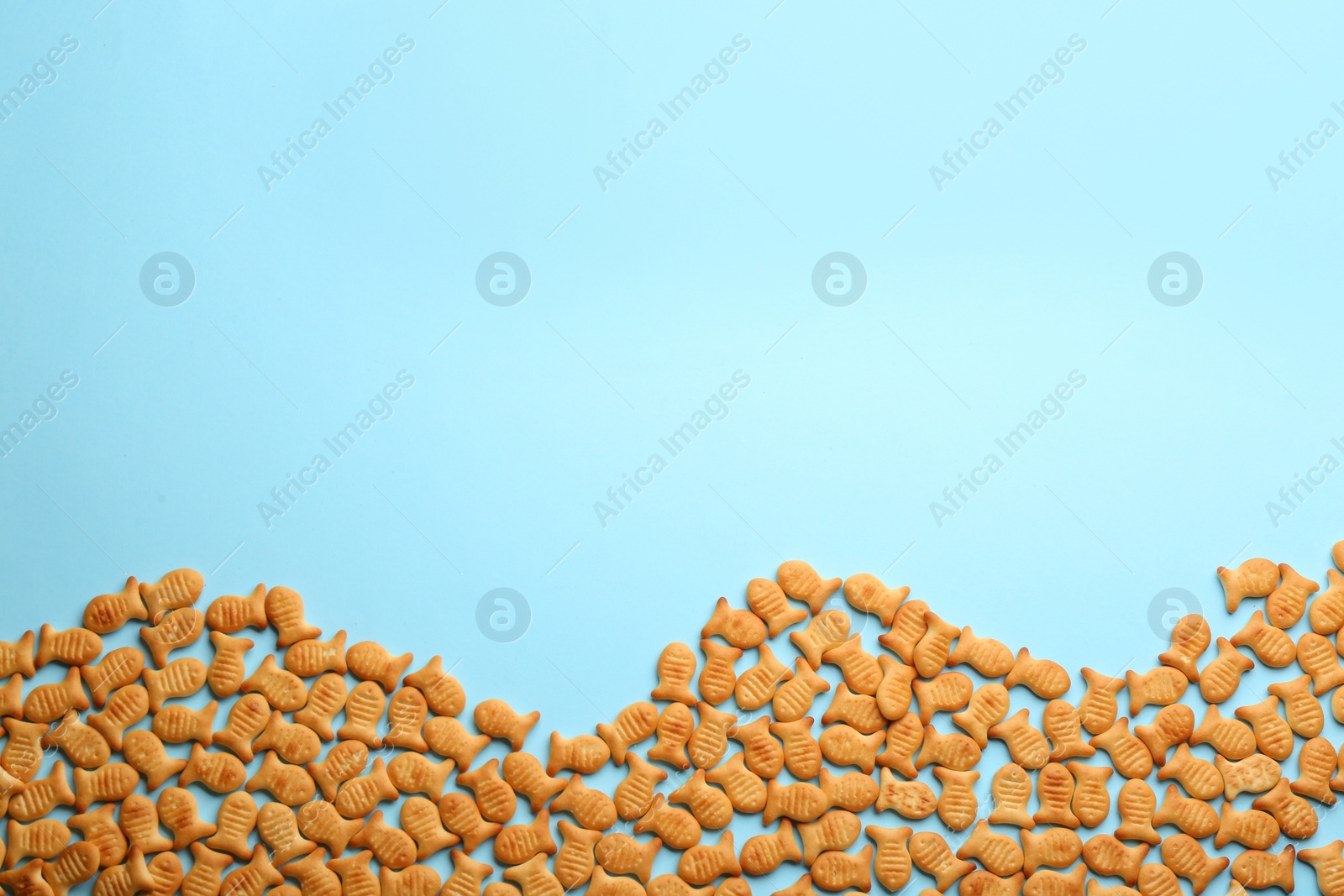 Photo of Delicious goldfish crackers on light blue background, flat lay. Space for text