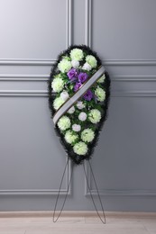 Photo of Funeral wreath of plastic flowers with ribbon near light grey wall indoors