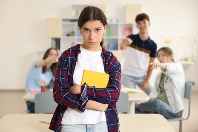 Photo of Teen problems. Students pointing at upset girl in classroom, selective focus