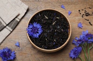 Photo of Dried cornflower tea and fresh flowers on wooden table, flat lay