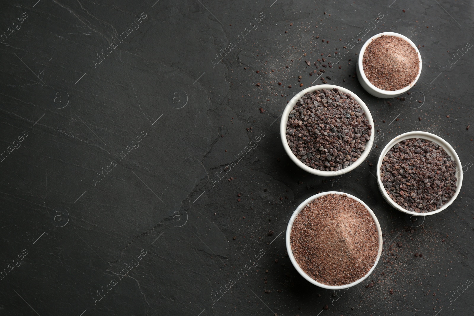 Photo of Black salt on dark slate table, flat lay. Space for text