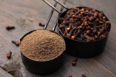 Aromatic clove powder and dried buds in scoops on wooden table, closeup