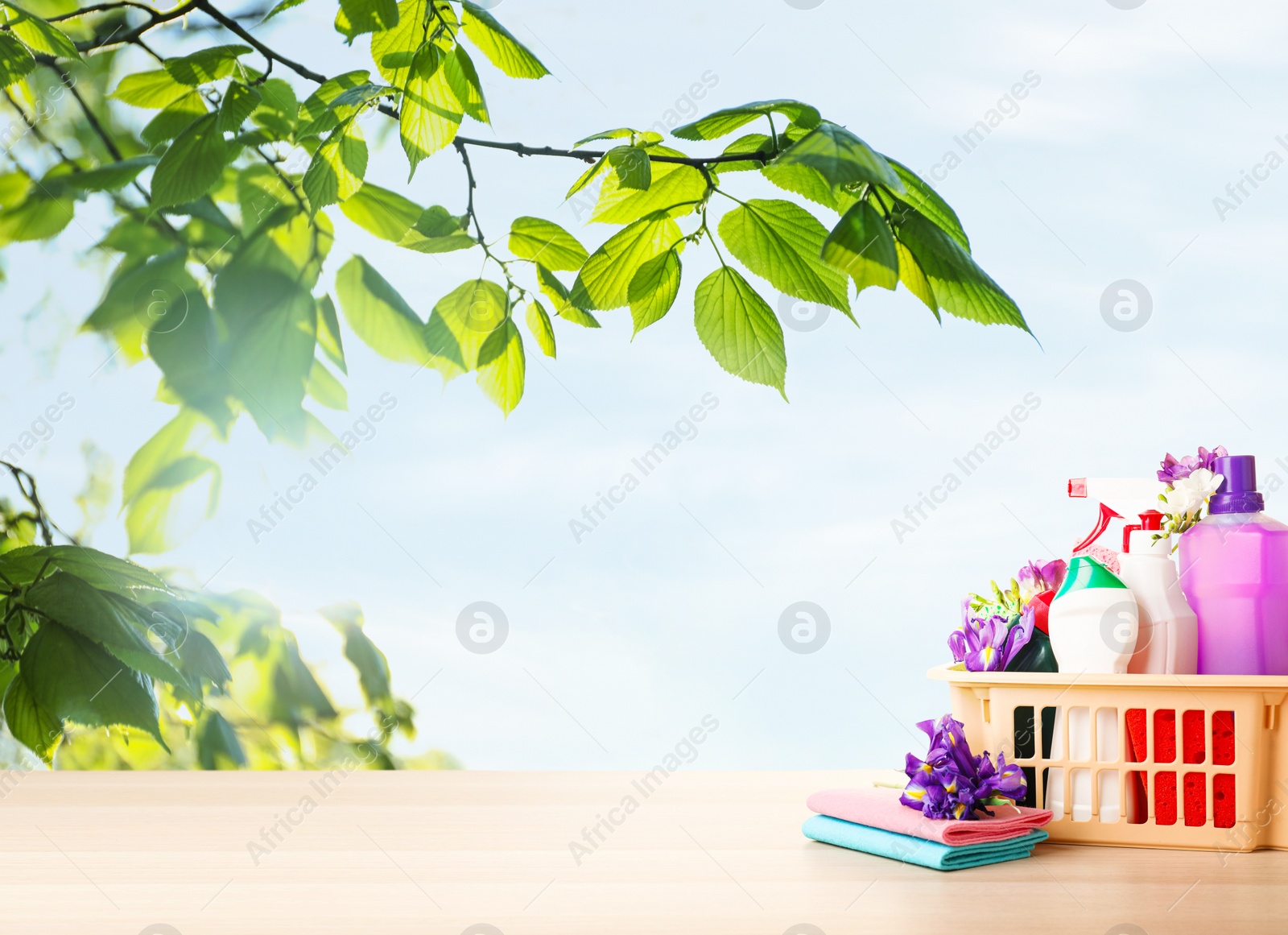 Image of Plastic basket with different detergents on wooden table, space for text. Spring cleaning concept 