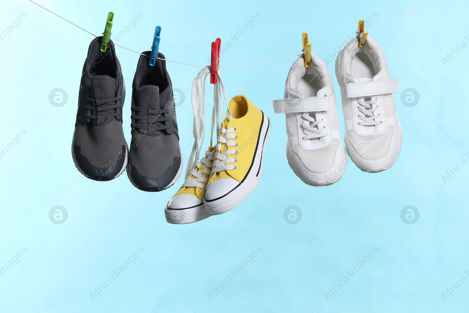 Photo of Different stylish sneakers drying on washing line against light blue background