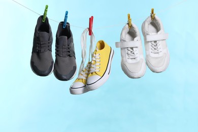 Photo of Different stylish sneakers drying on washing line against light blue background