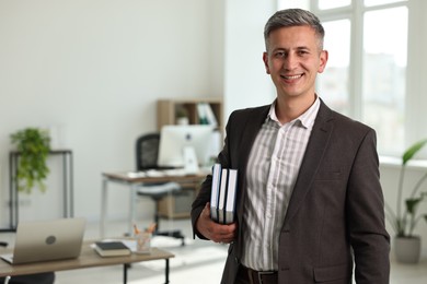 Happy man with notebooks in office, space for text