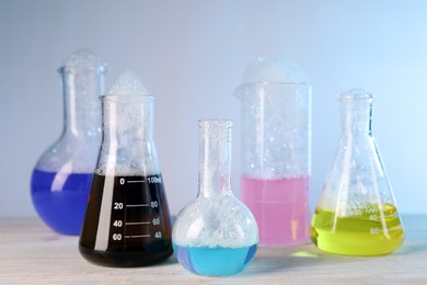 Photo of Laboratory glassware with colorful liquids on white wooden table against light blue background. Chemical reaction