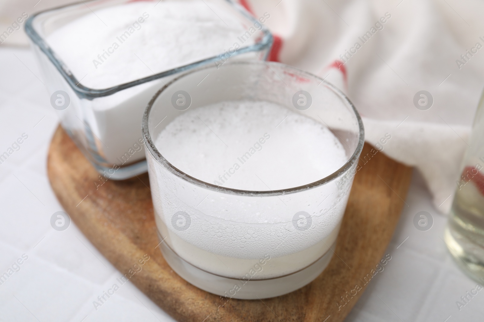 Photo of Chemical reaction of vinegar and baking soda in glass bowl on white table, closeup