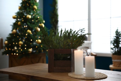 Photo of Burning candles and fir branches on wooden table in room decorated for Christmas