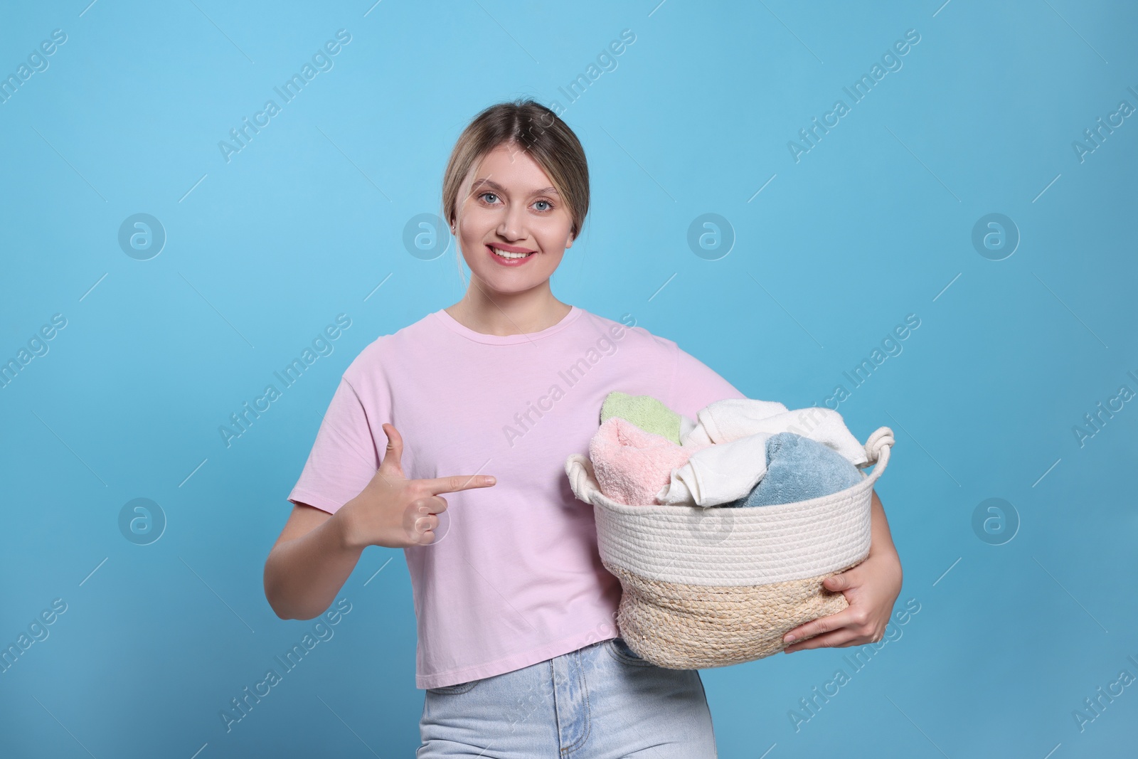 Photo of Happy woman with basket full of laundry on light blue background