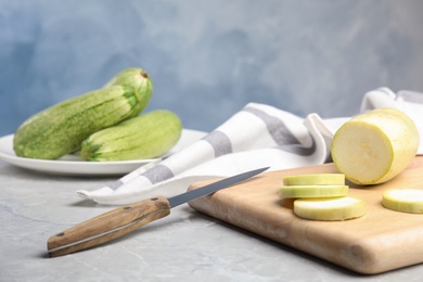 Photo of Wooden board with fresh ripe zucchini and knife on grey table. Space for text