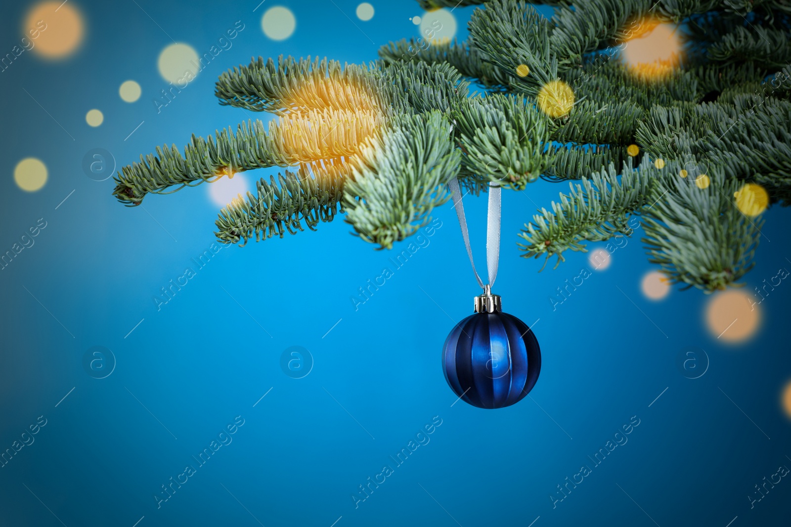 Photo of Beautiful Christmas ball hanging on fir tree branch against light blue background, bokeh effect